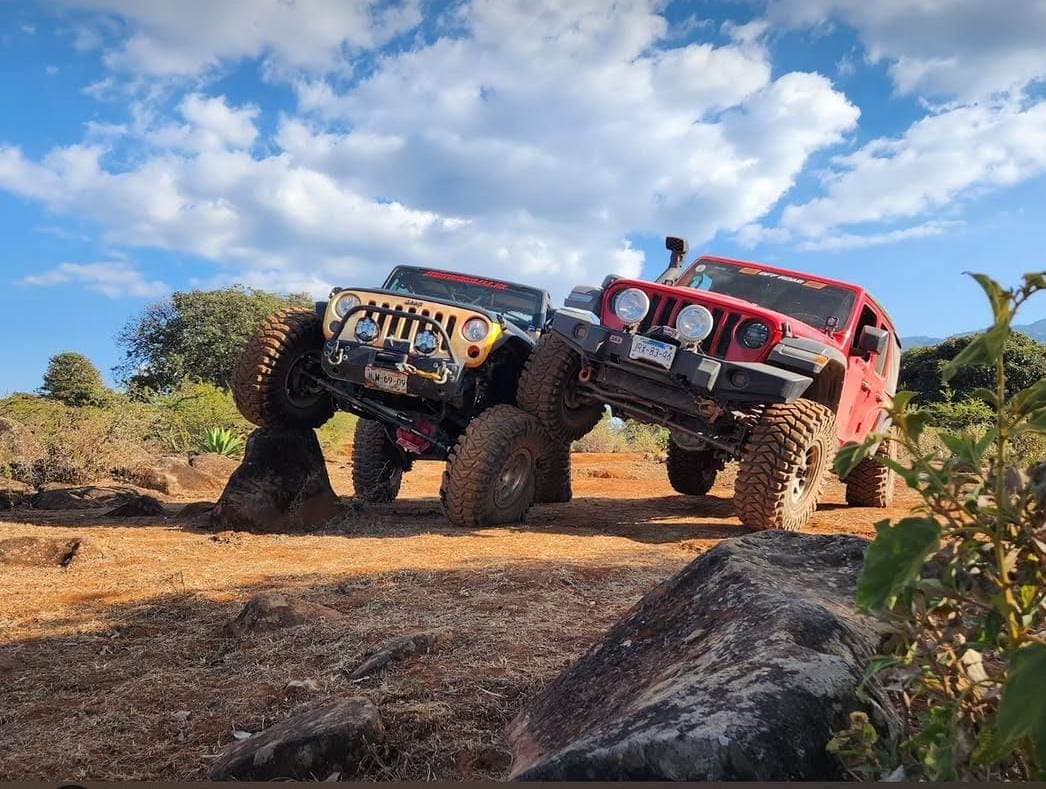 Dos Jeep Wrangler trepando una formación rocosa bajo cielo azul