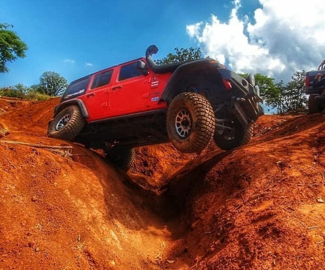 Jeep Wrangler roja bajando una zanja de tierra roja